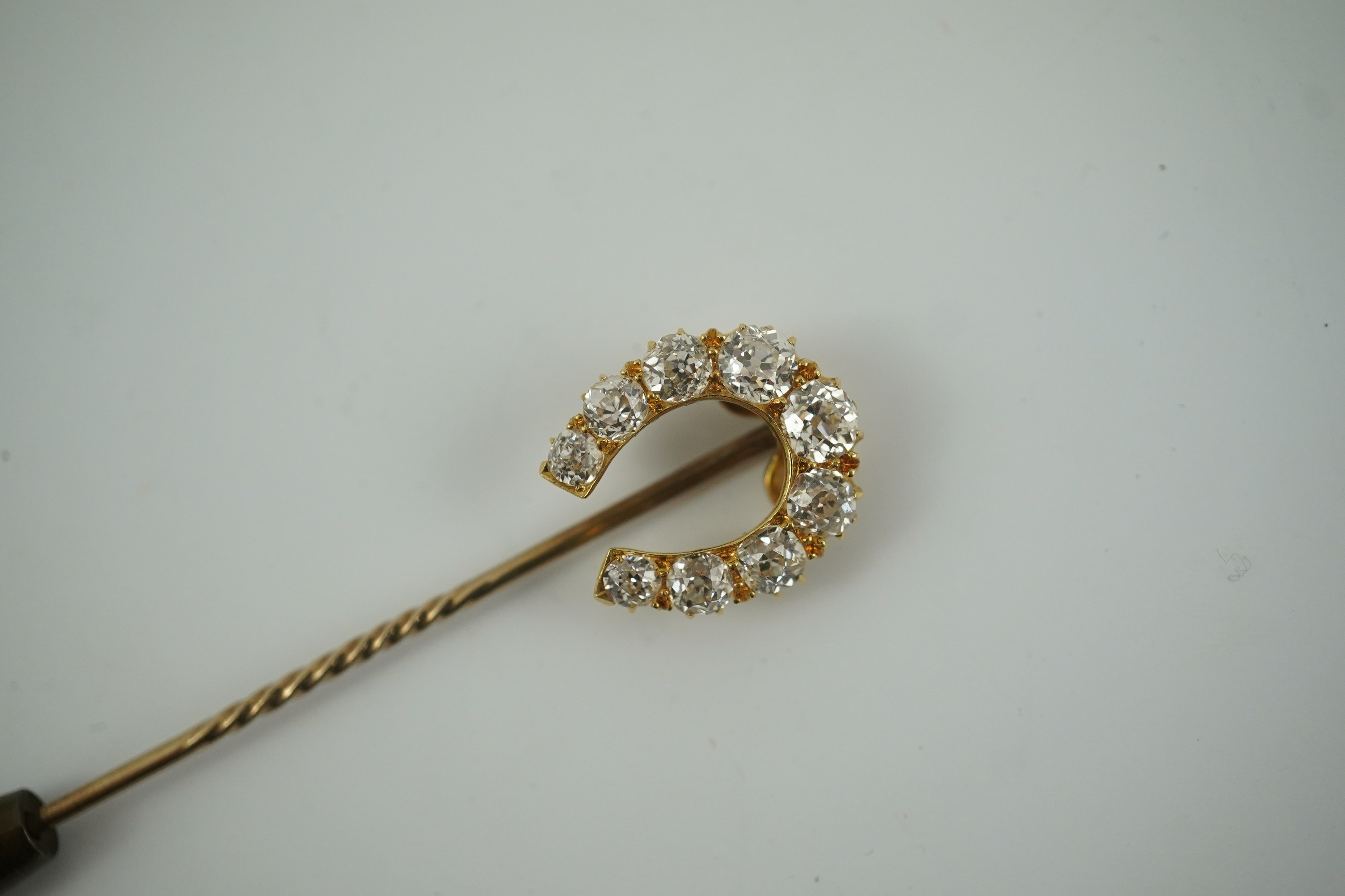 An early 20th century gold and nine stone graduated old cut diamond set horseshoe stick pin